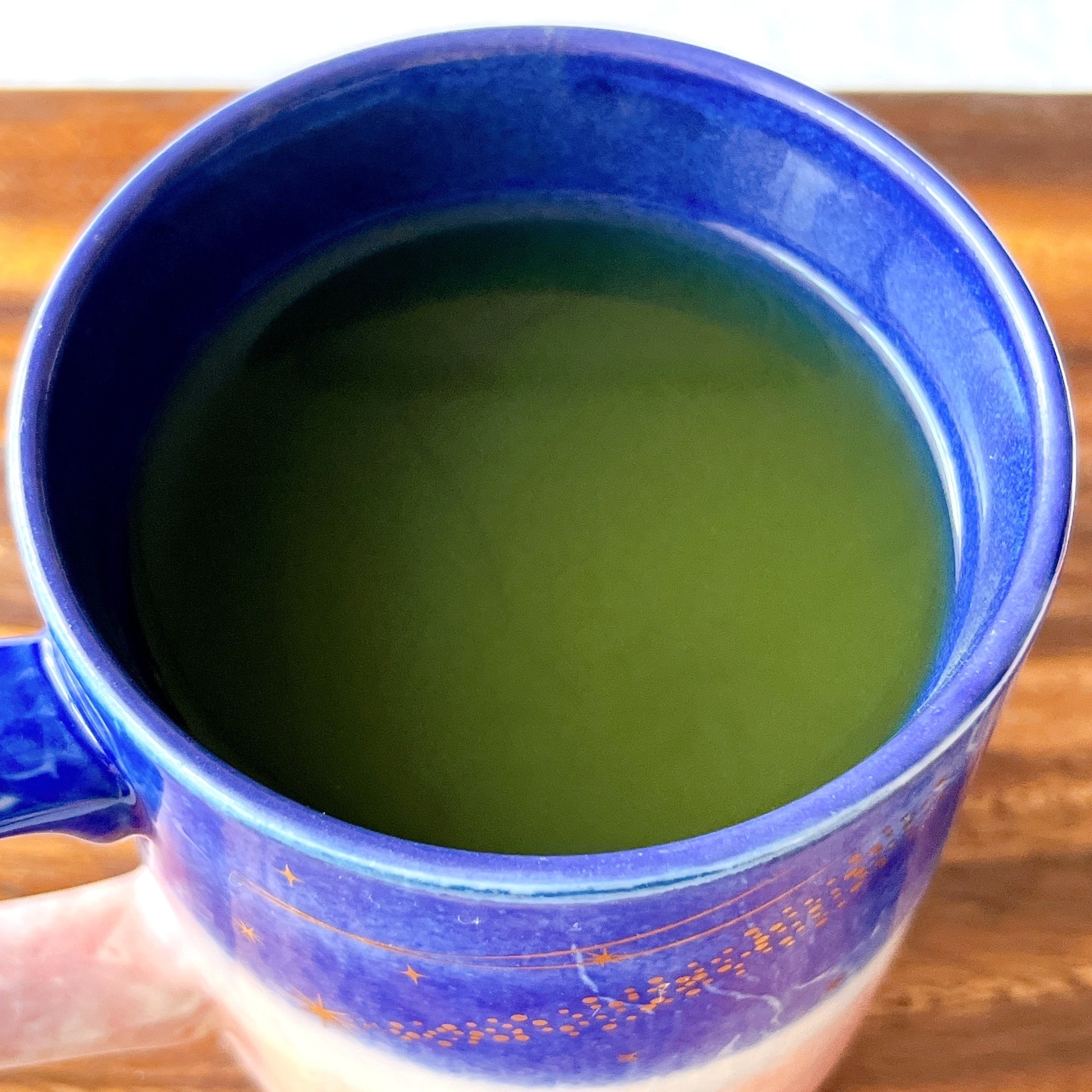 青いマグカップに入った緑の飲み物がテーブル上に置かれている。