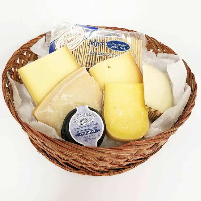 Assorted food and crackers successful a wicker basket, featuring Cheddar and Parmesan, suitable for gifting
