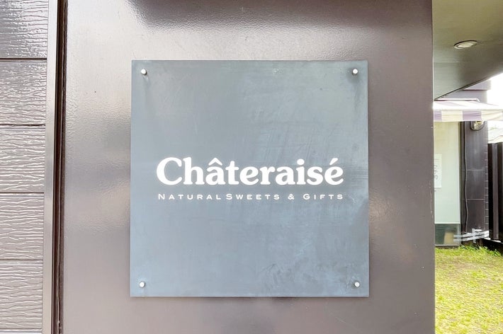 シャトレーゼの看板が建物の壁に取り付けられている様子。近くの緑が見える。