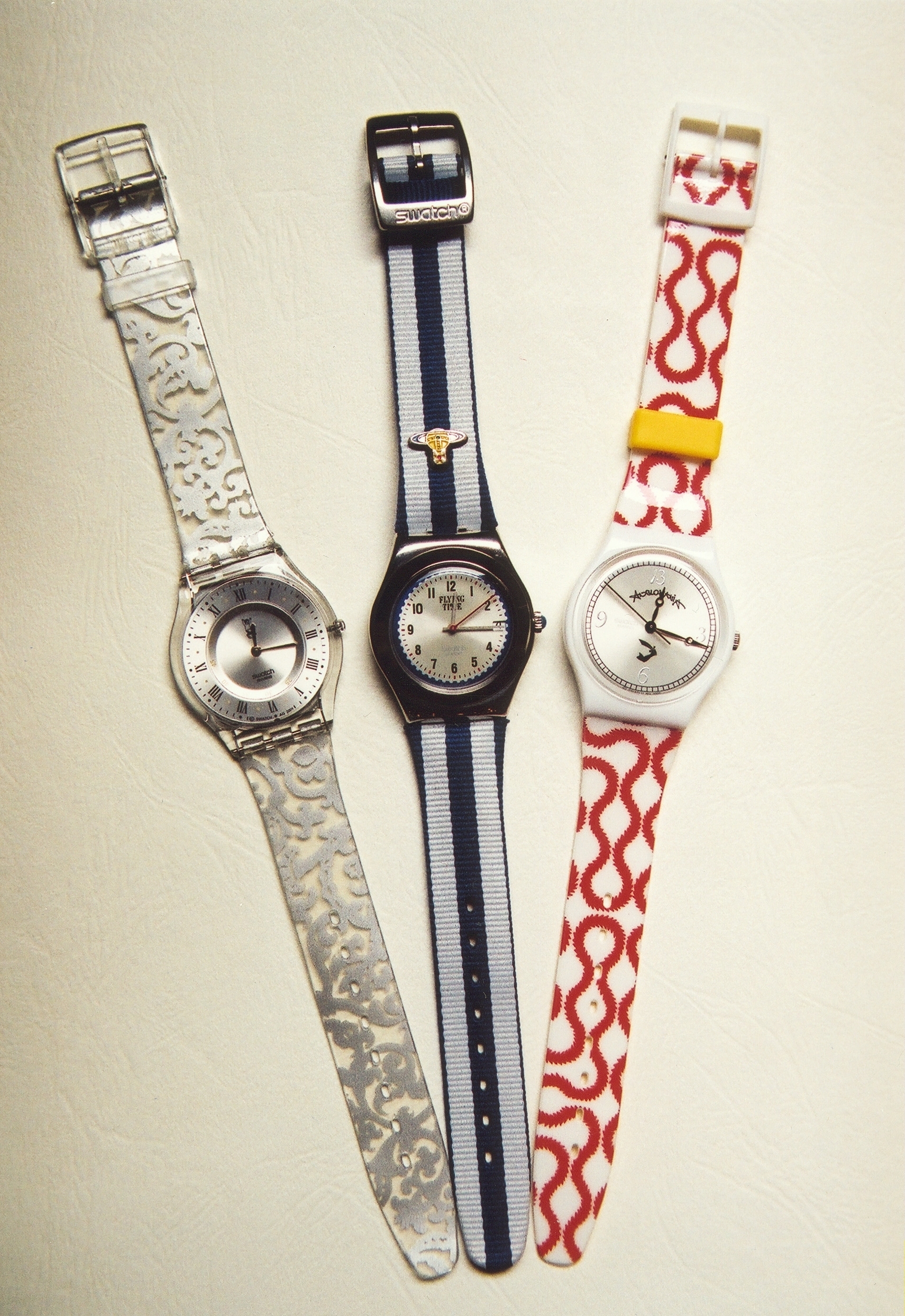 Three Swatch wristwatches with unique band patterns: intricate, striped with emblem, and wavy red and white design, displayed on a neutral background