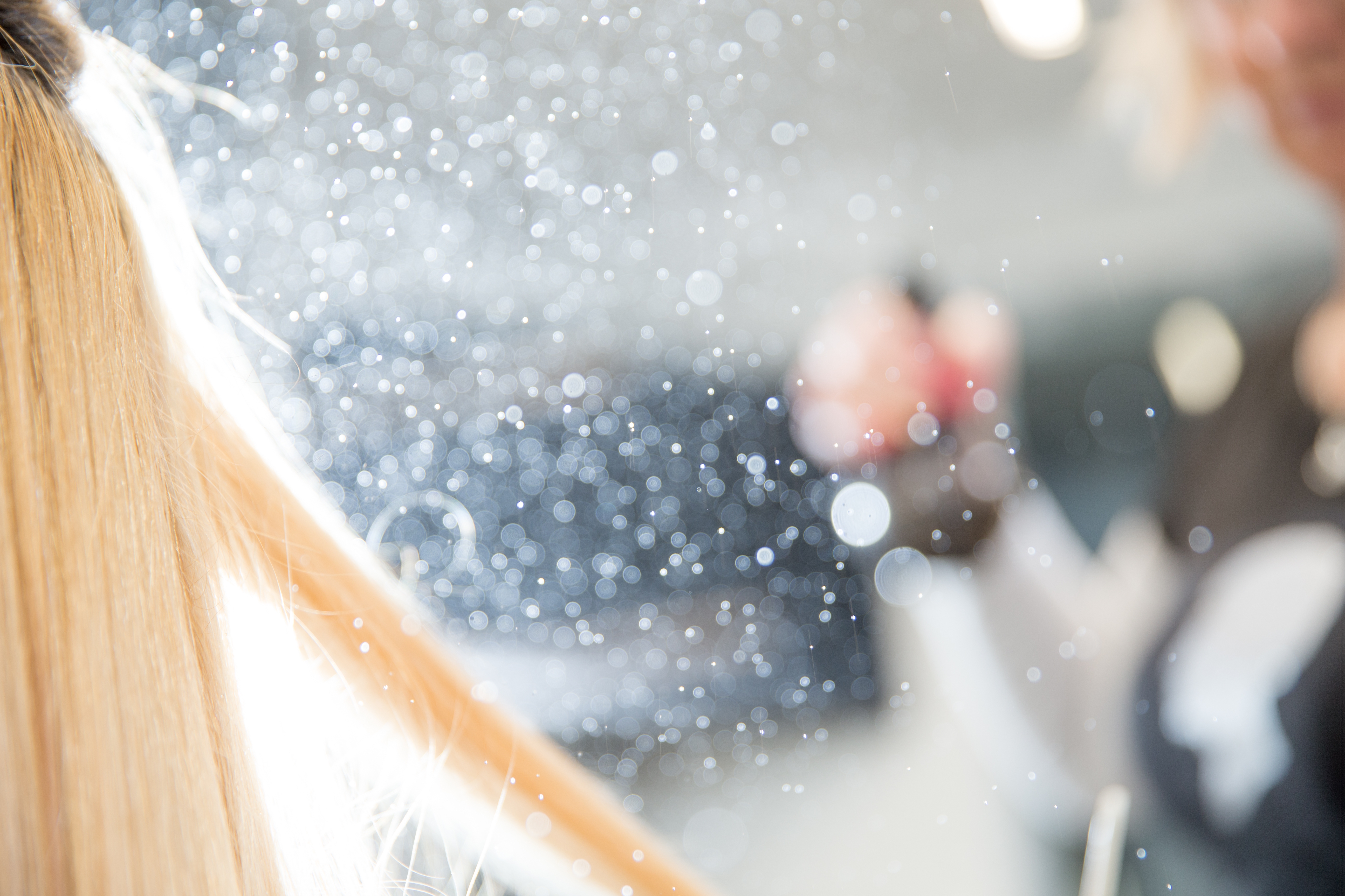 A person sprays hair with mist in a salon, creating a sparkling effect in the air