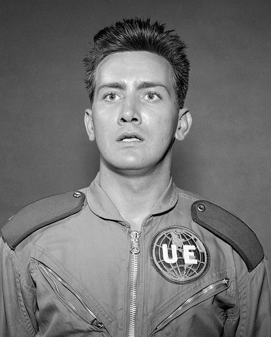 Person successful  a futuristic jumpsuit with UE emblem, looking startled against a plain background