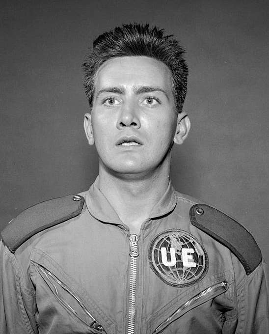 Person in a futuristic jumpsuit with UE emblem, looking startled against a plain background
