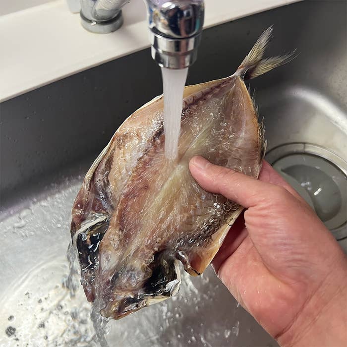 シンクで魚を流水で洗っている手。