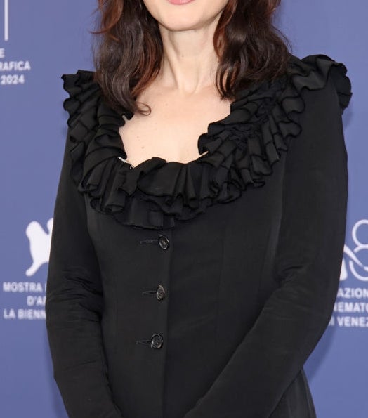 Person in elegant ruffled dress stands in front of a blue event backdrop, smiling