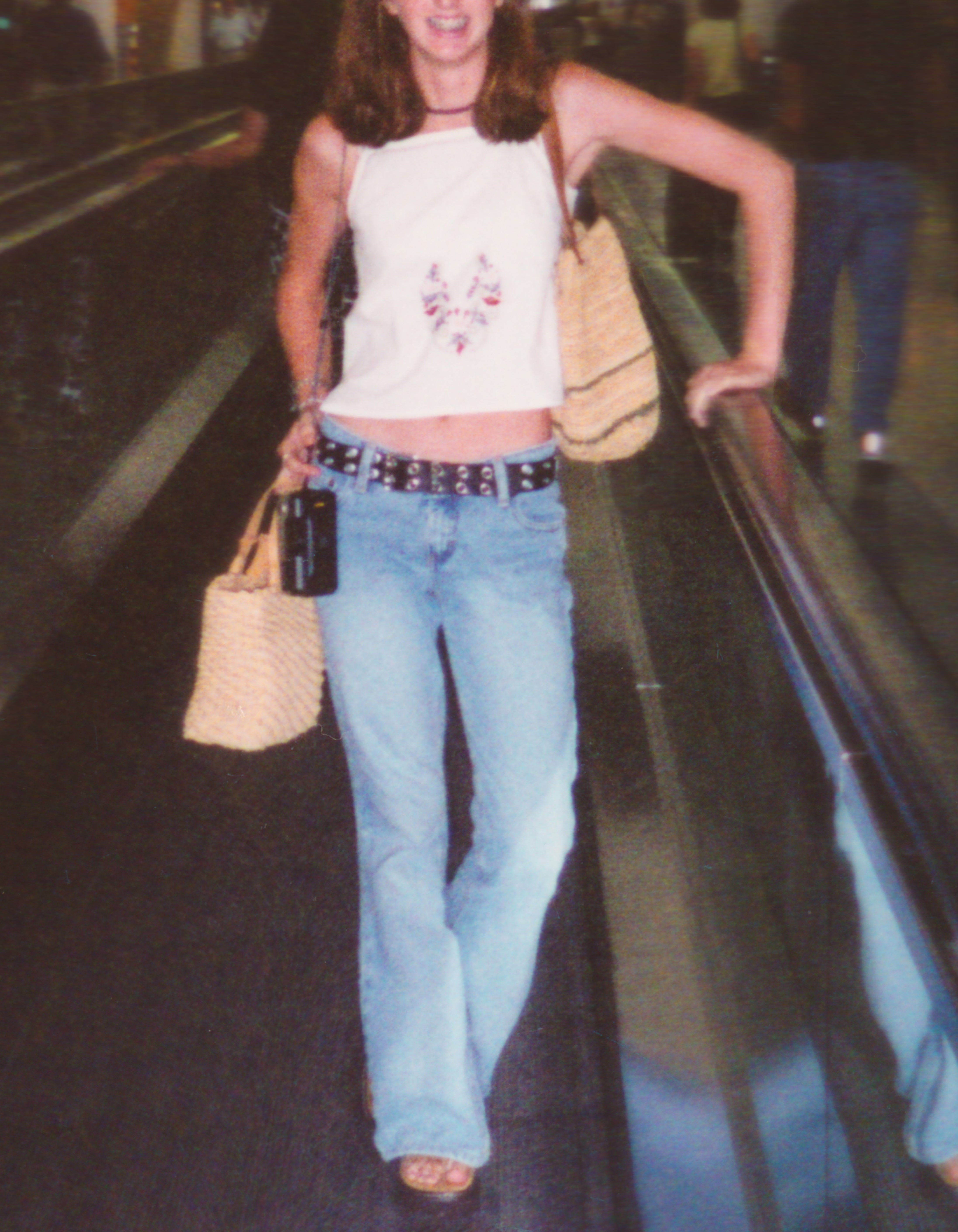 Person walking in an airport, wearing a sleeveless top, jeans, and carrying a woven handbag