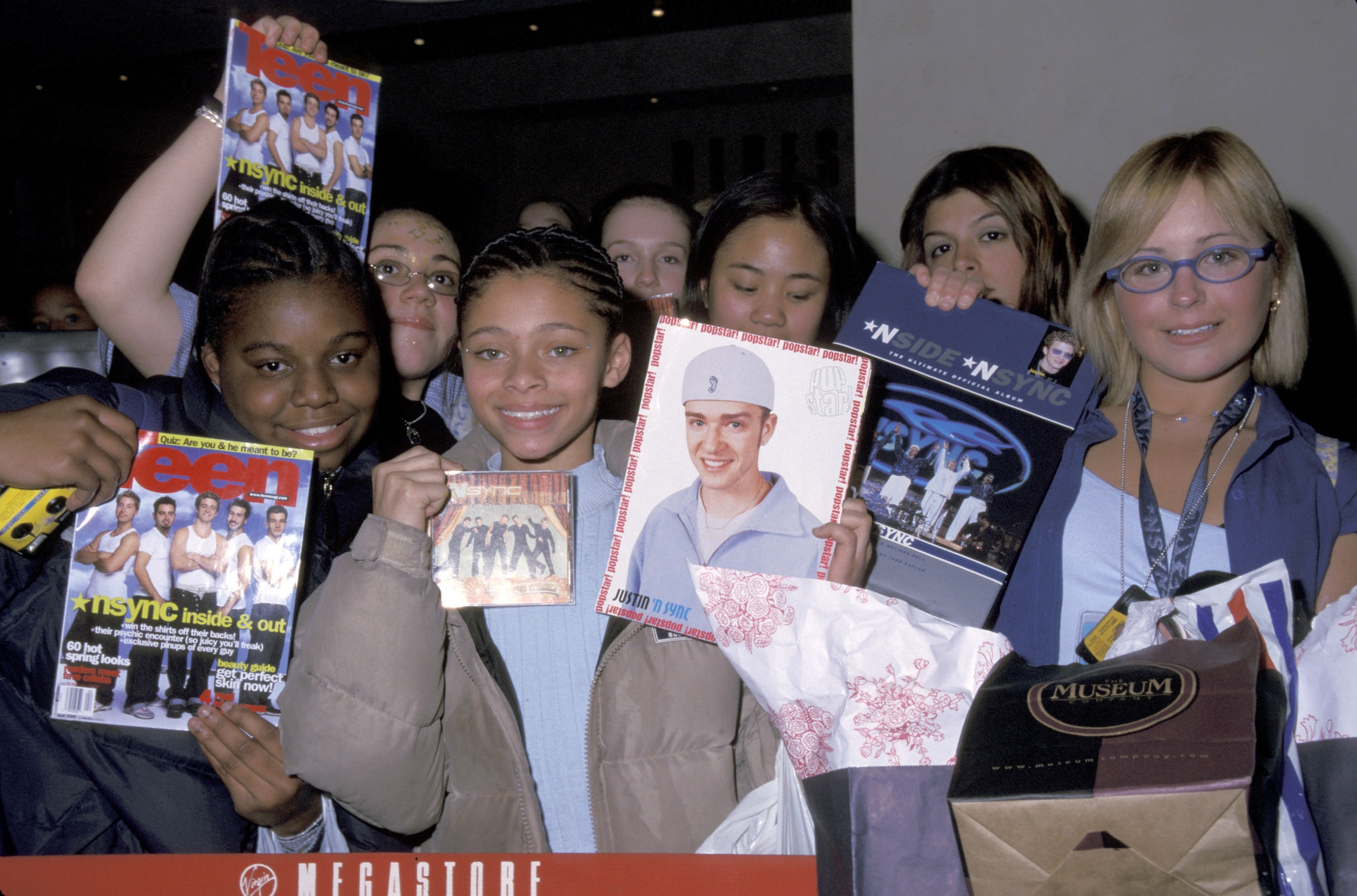Group of young people holding magazines and posters of pop bands from the early 2000s, smiling and excited