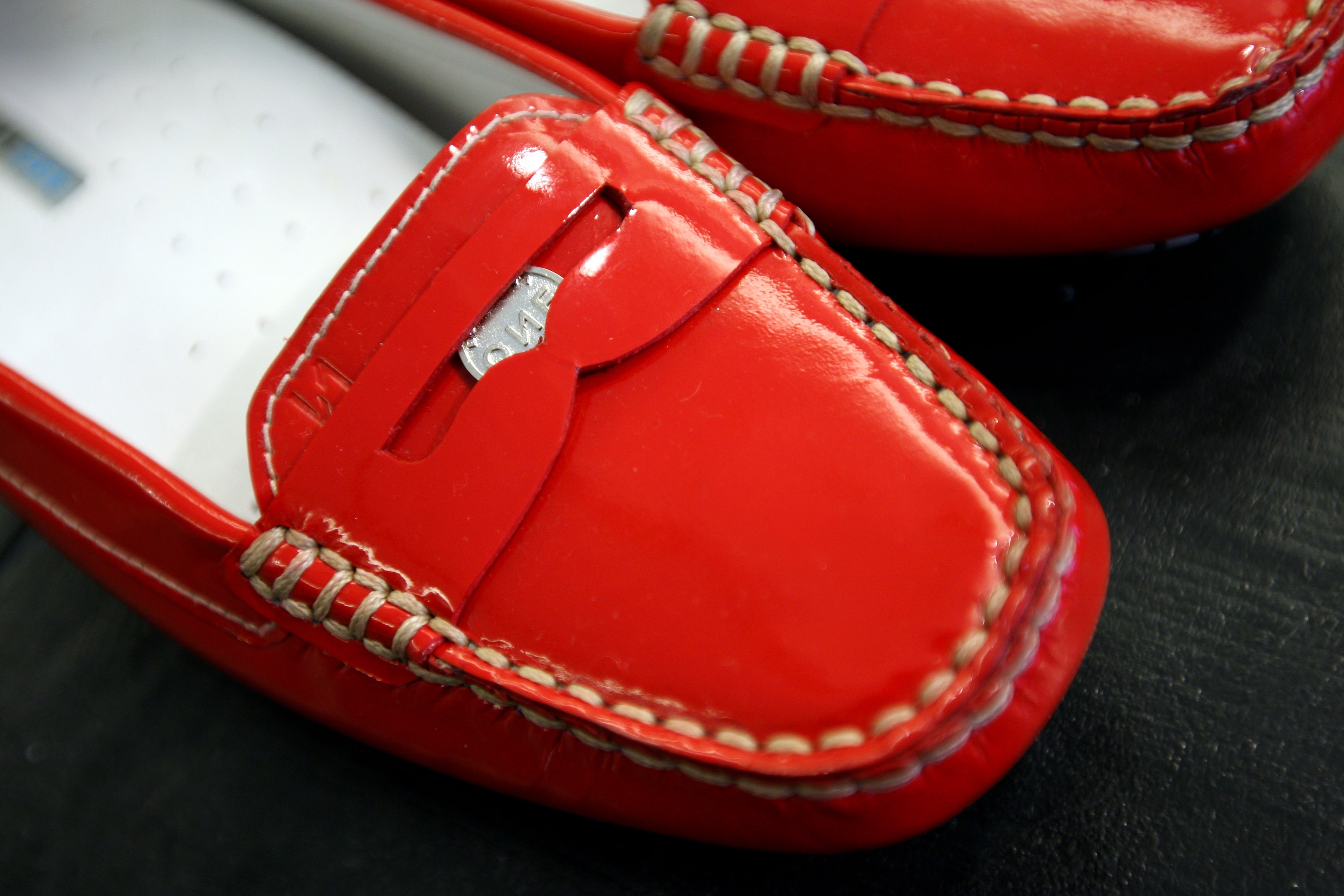 Close-up of a glossy red loafer with stitching details and a decorative buckle on the upper part