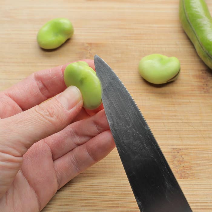 手に持ったそら豆を、ナイフで切ろうとしている様子。