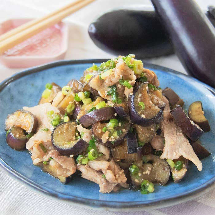 ナスと豚肉の甘辛炒めが青い皿に盛られている。後ろに箸とナスが見える。