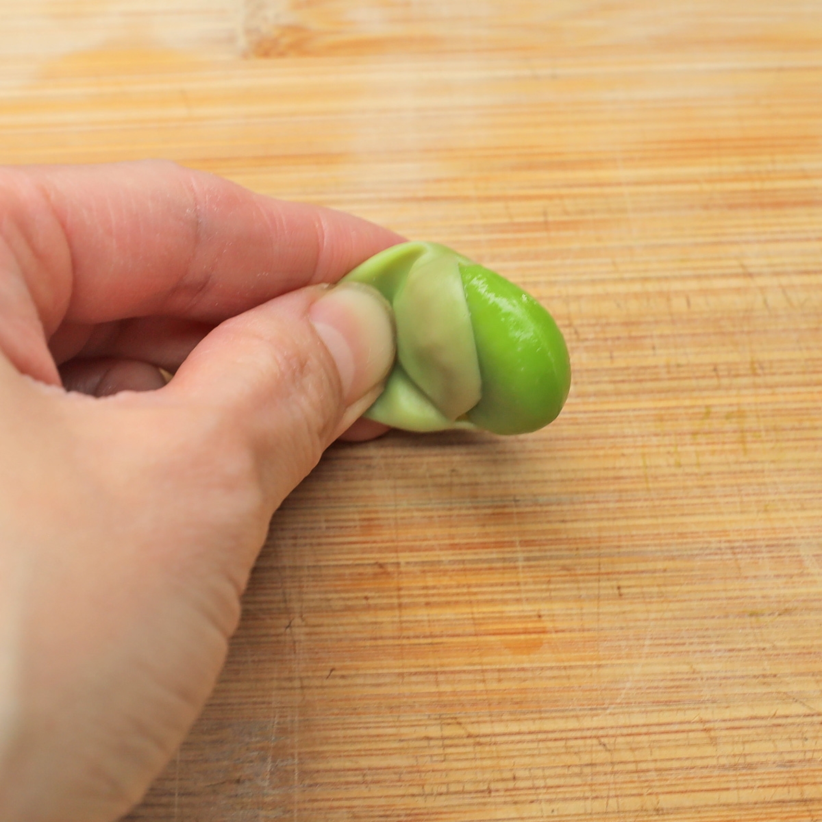 手が木のまな板の上で豆のさやを剥いている様子。