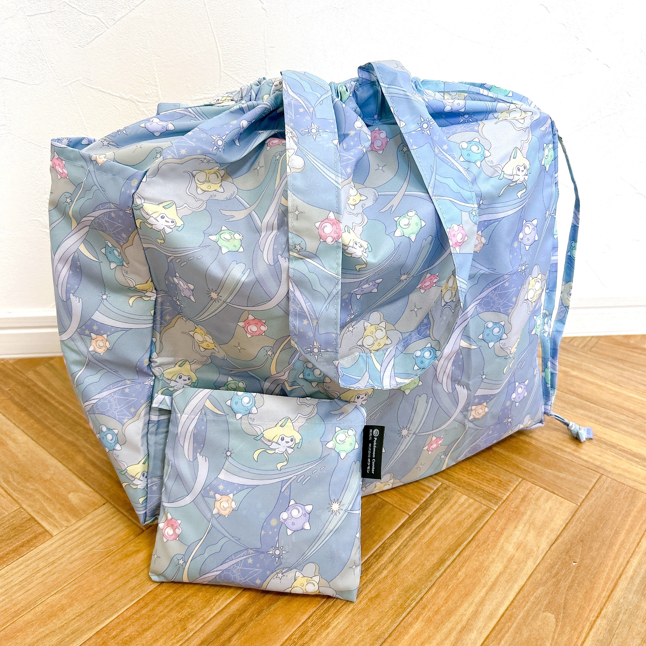 アニメキャラクターが描かれた大きなトートバッグと小さなポーチが床に置かれている。