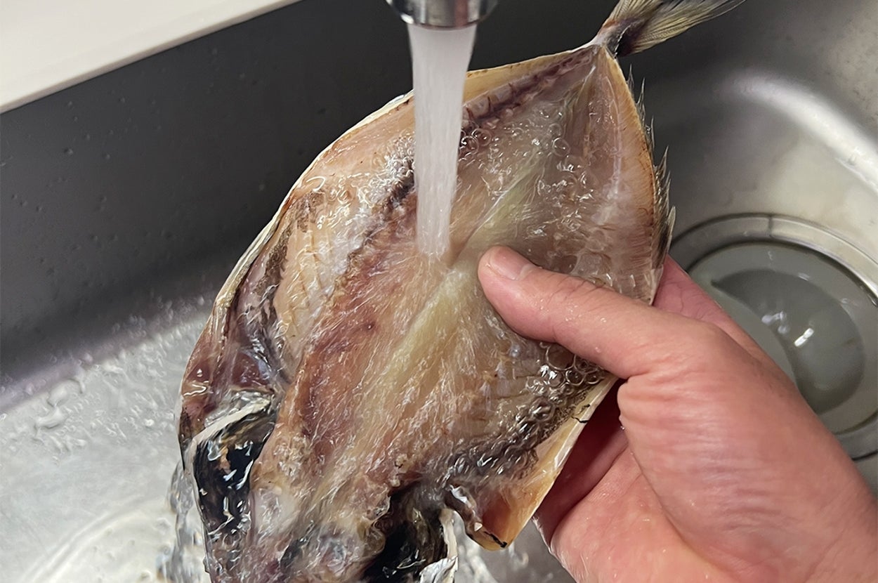 手で持たれた魚がシンクで水をかけられて洗われている。