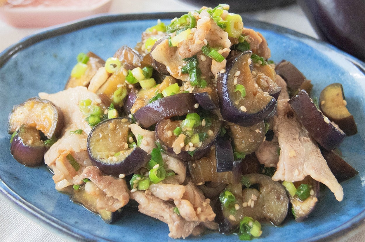 ナスと豚肉の甘辛炒めが青い皿に盛られている。後ろに箸とナスが見える。