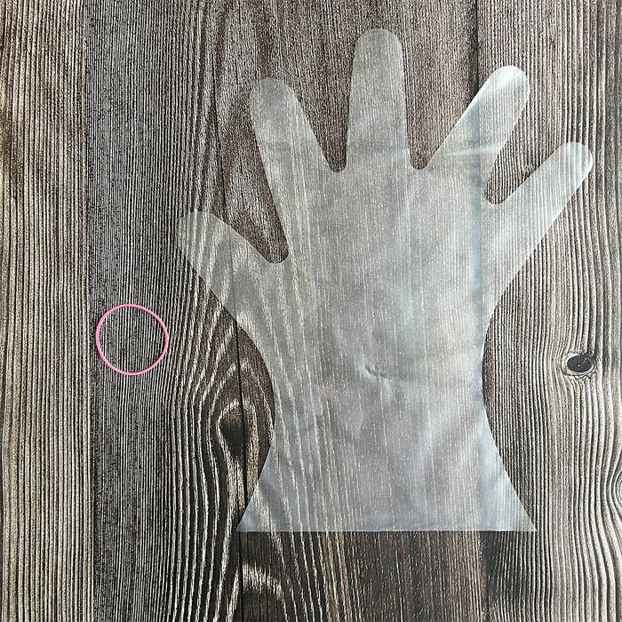 木製の表面に手袋型の透明素材と小さなピンクのゴムバンド。