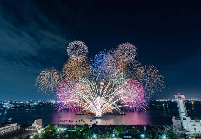 夜空を背景に大規模な花火が打ち上がる美しい光景。都市の灯りが遠景に見える。