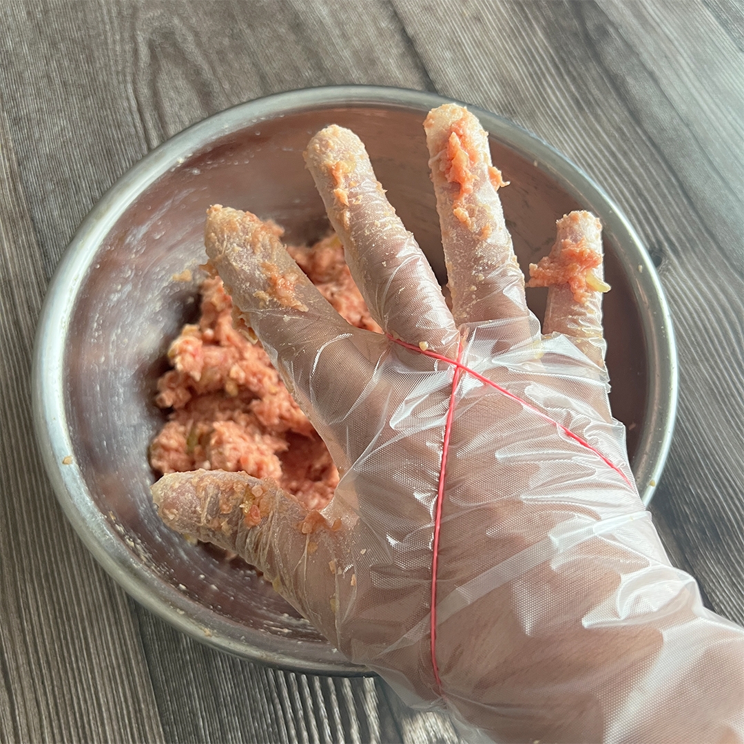 調理用手袋をした手で肉をこねている様子。ボウルに入ったひき肉のミックス。