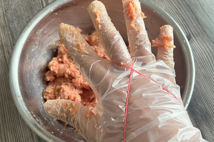手袋をした手がボウルに入った肉をこねている様子。