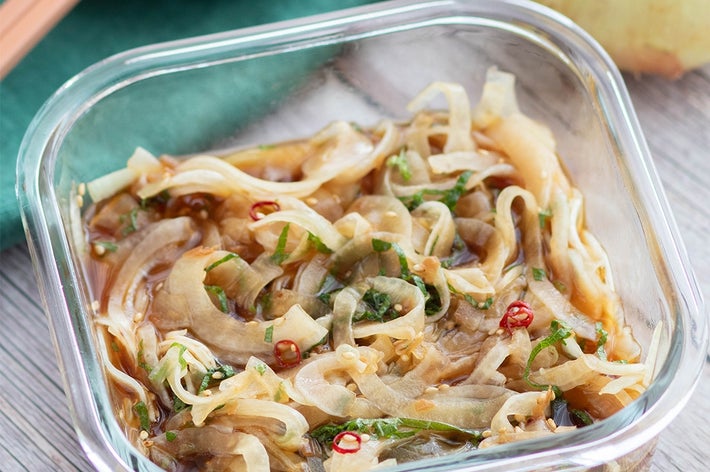 玉ねぎと唐辛子が入ったマリネサラダがガラス容器に盛られている。後ろにタマネギと緑の布が見える。