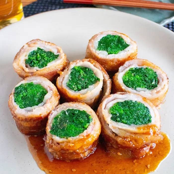 肉で巻かれた緑の野菜が綺麗に盛り付けられたお皿。ソースがかかっており、食欲をそそる一品。