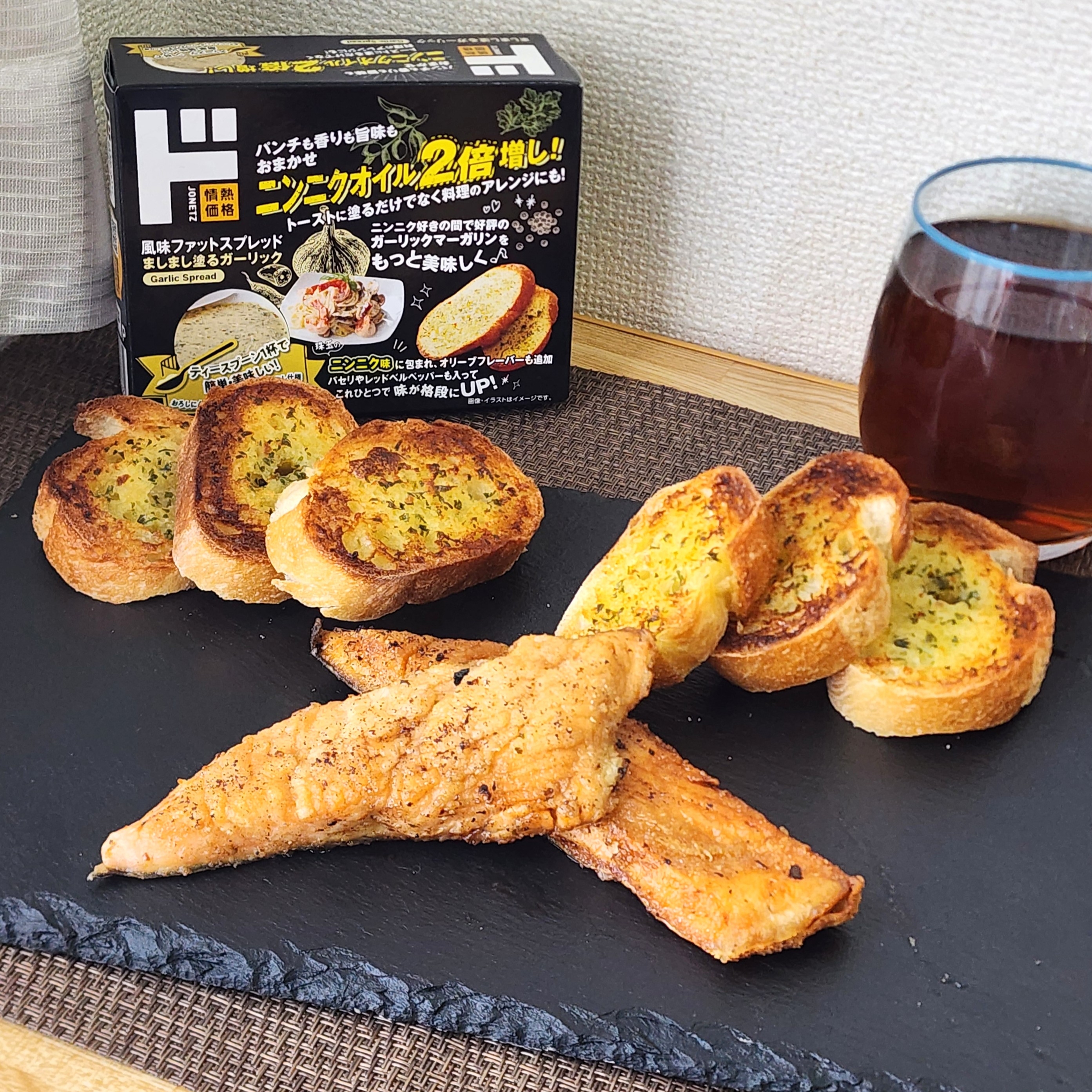 ガーリックトーストとグリルチキンの盛り合わせ。背景に食品パッケージと飲み物がある。
