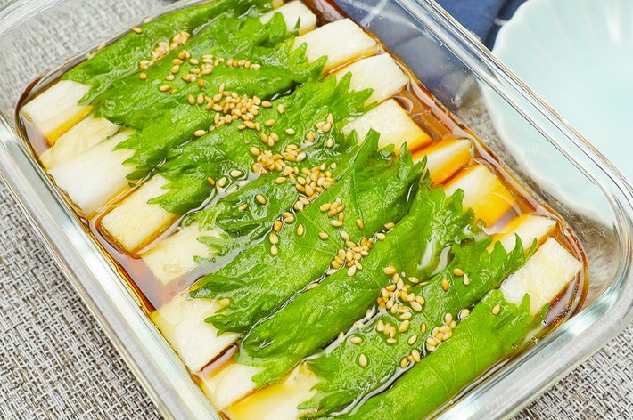 ガラス容器に並べられたシソで覆われた料理。ゴマがトッピングされ、ソースがかかっています。