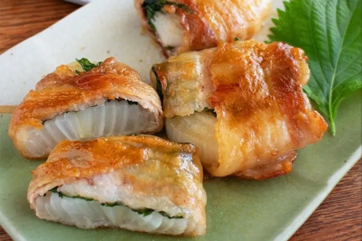 肉巻き大葉の焼いた料理が皿に盛られ、横に緑の葉が添えられている。