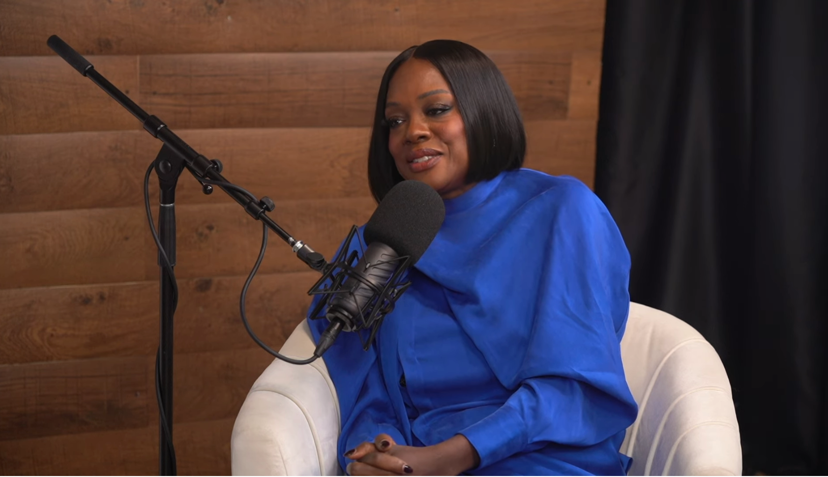 Person sits in a modern recording studio with a microphone, wearing a sleek outfit