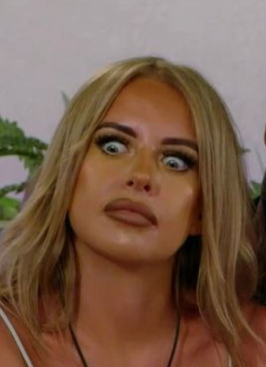 A surprised person with wide eyes and open lips, sitting indoors, likely reacting to something unexpected
