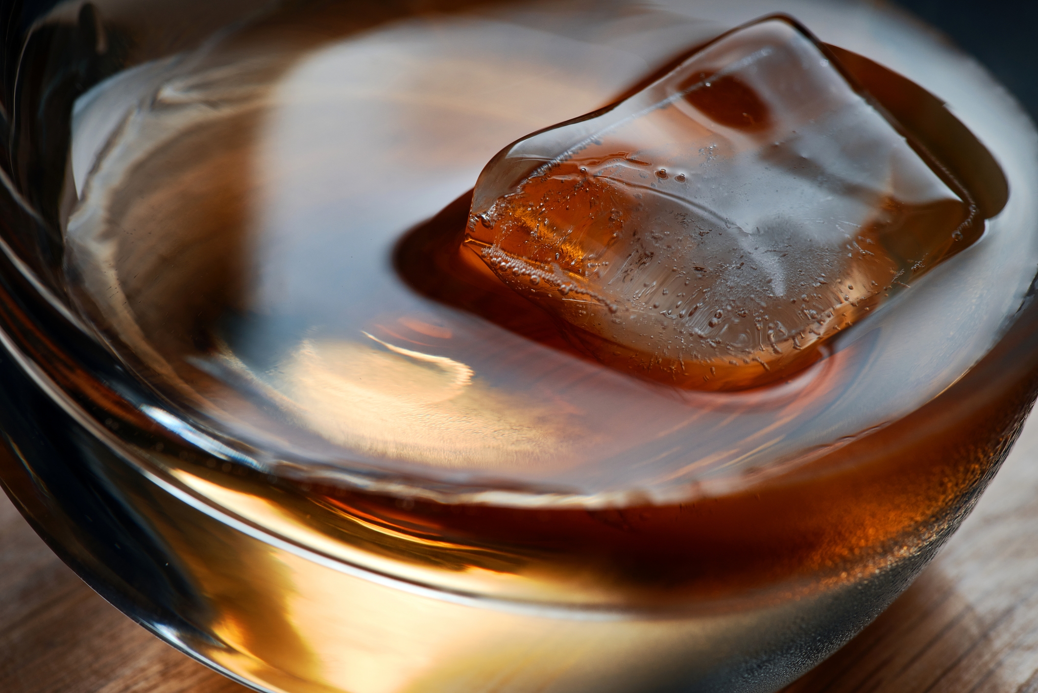 Close-up of a glass with a single ice cube in a brown liquid