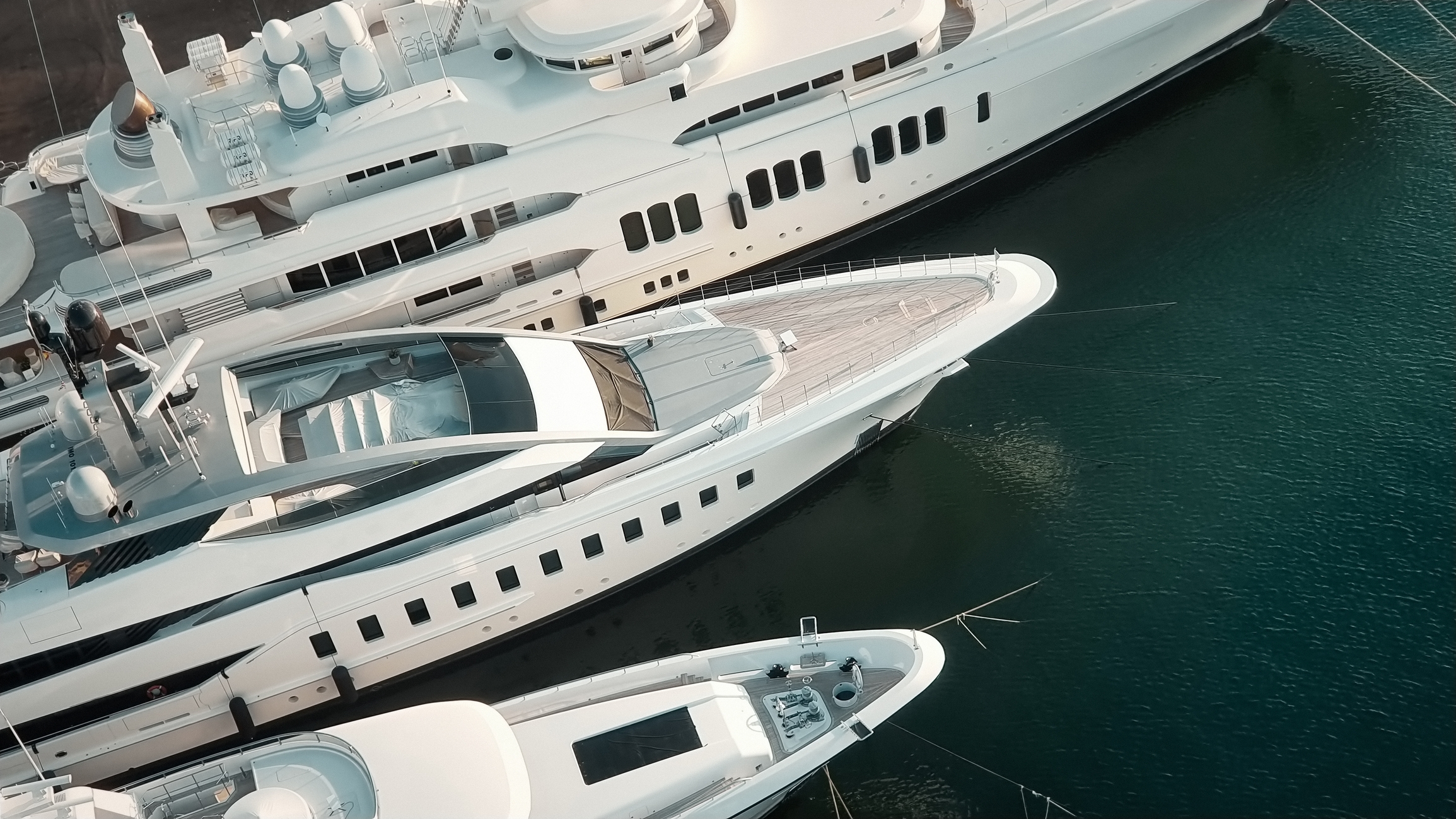 Three luxury yachts docked in a marina, showcasing opulence and wealth in the boating industry