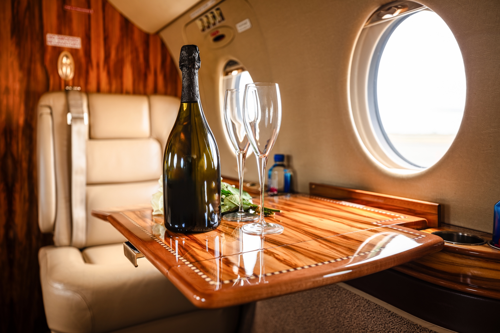 Private jet interior with a fold-out wooden table displaying a bottle of champagne and two glasses, suggesting luxury travel