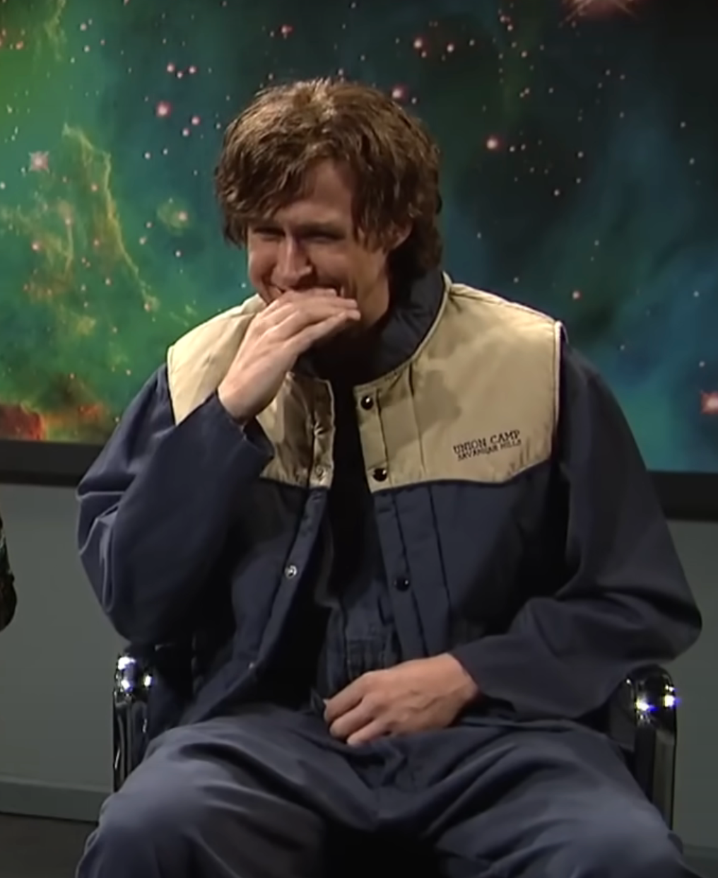 Person sitting happily in a space-themed setting, wearing a casual jacket and shirt, with a galaxy backdrop, conveying a sense of joy