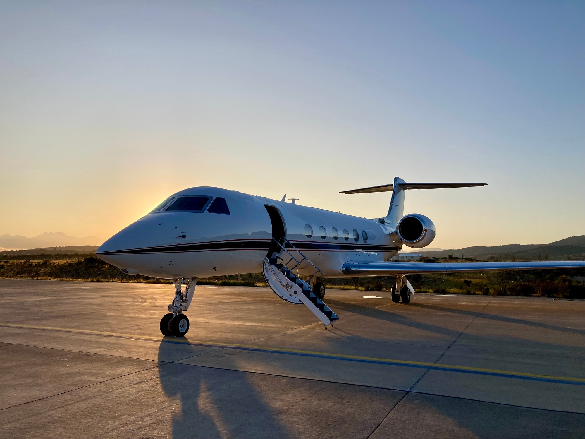 Private jet parked on tarmac at sunset, set against a clear sky and distant landscape