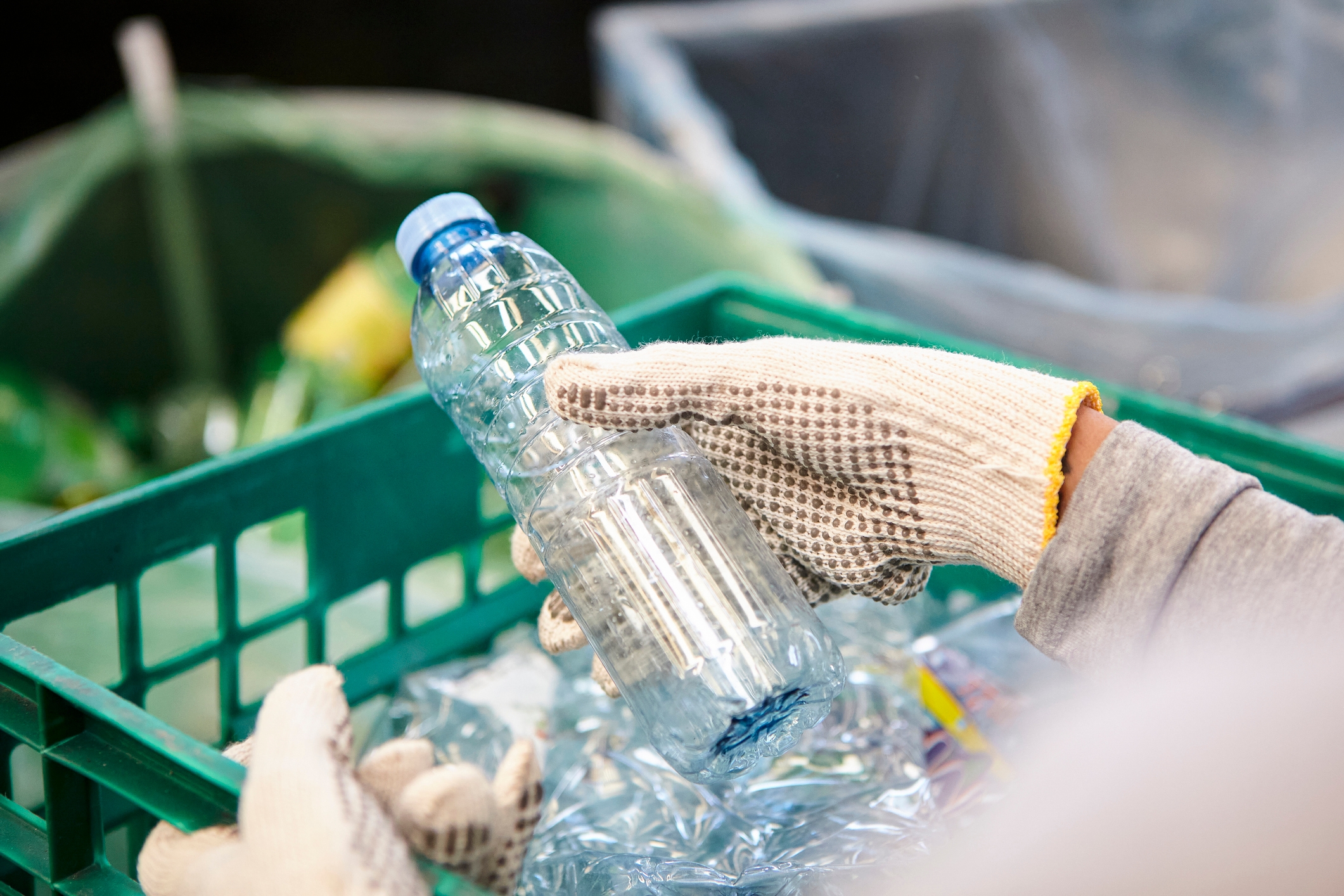 Person with gloves holding a plastic bottle over a recycling bin