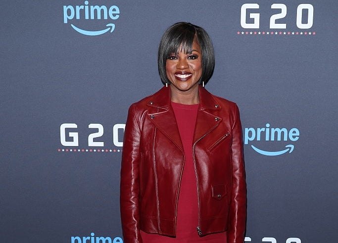 Person in a stylish red leather jacket and dress at a Prime event, standing on a photo call backdrop