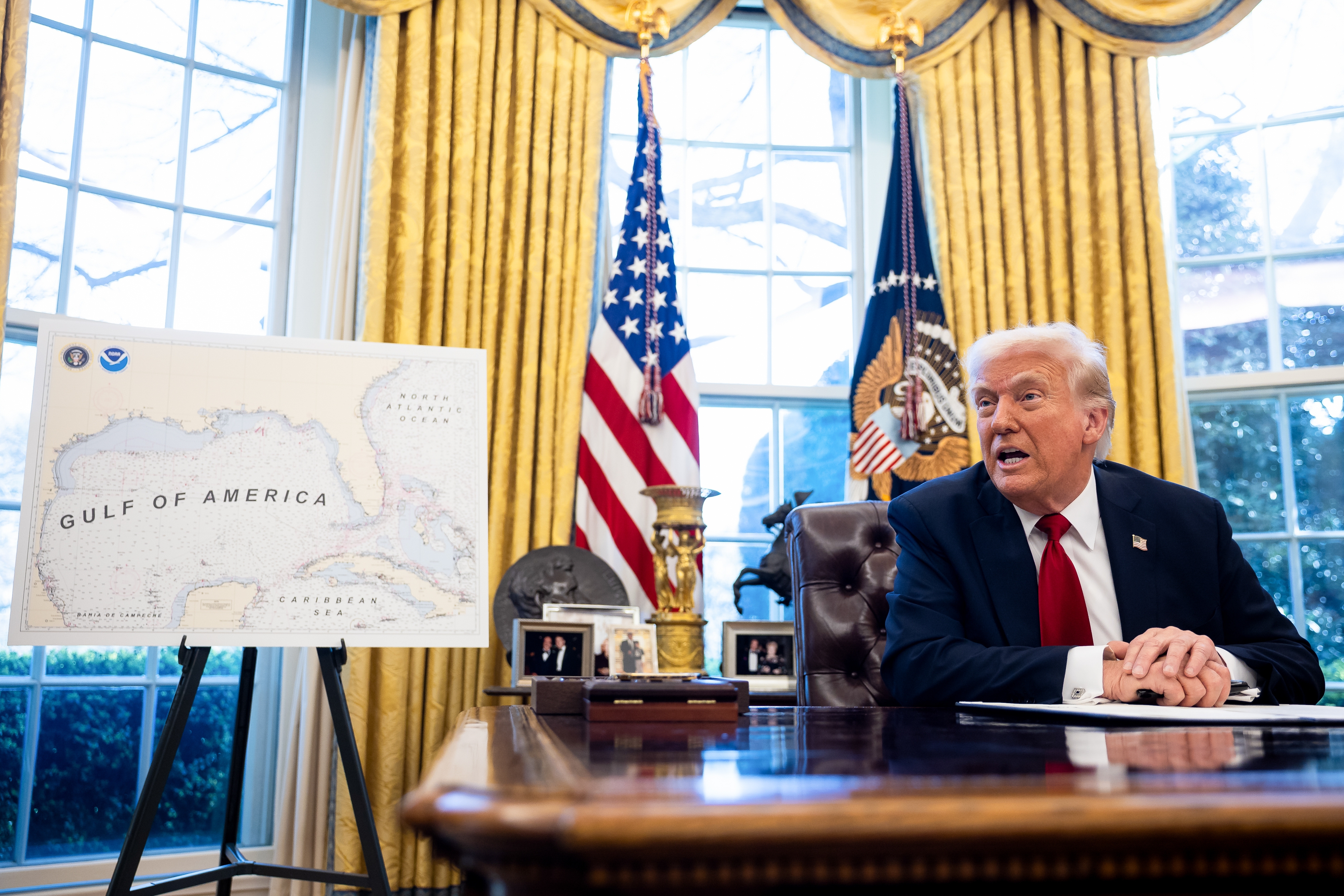 A person sits at a desk in an office with flags behind them, next to a map labeled "Gulf of America."