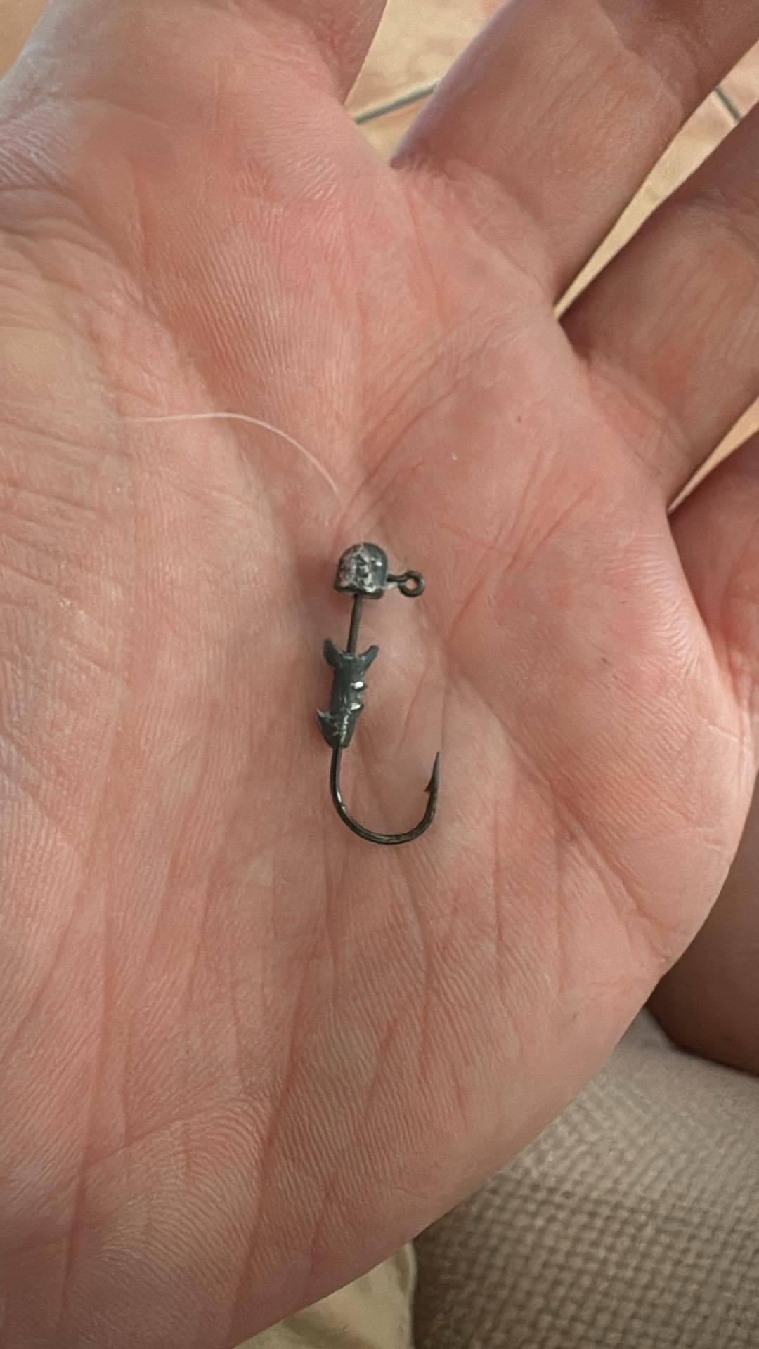 A person holds a fishing hook with a weighted jig head in their palm