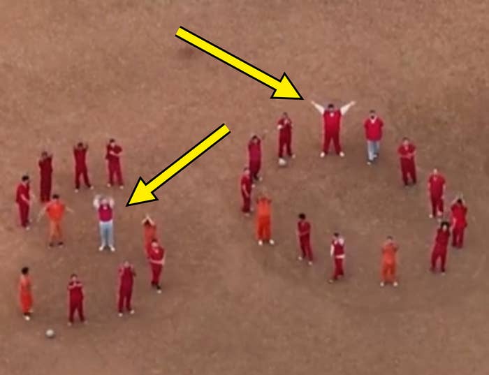 People arranged on a field spelling "SOS" with their bodies, wearing red and orange outfits