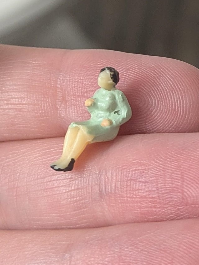 Tiny figurine resembling a person in a dress, seated on a fingertip