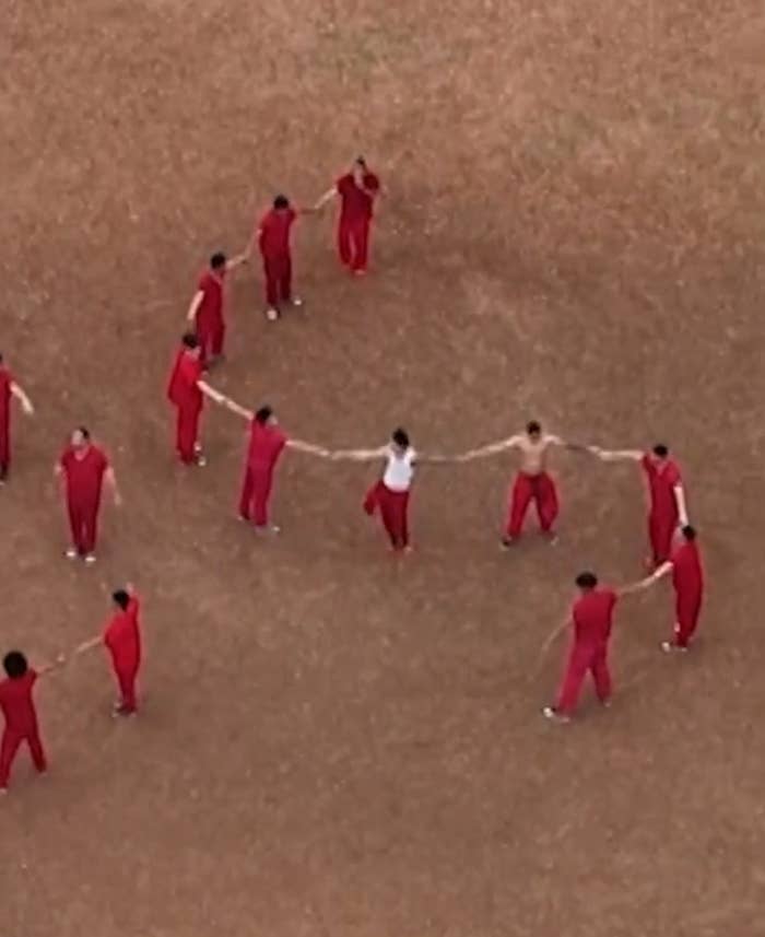 People in red outfits form a circle on a field, holding hands in a coordinated display