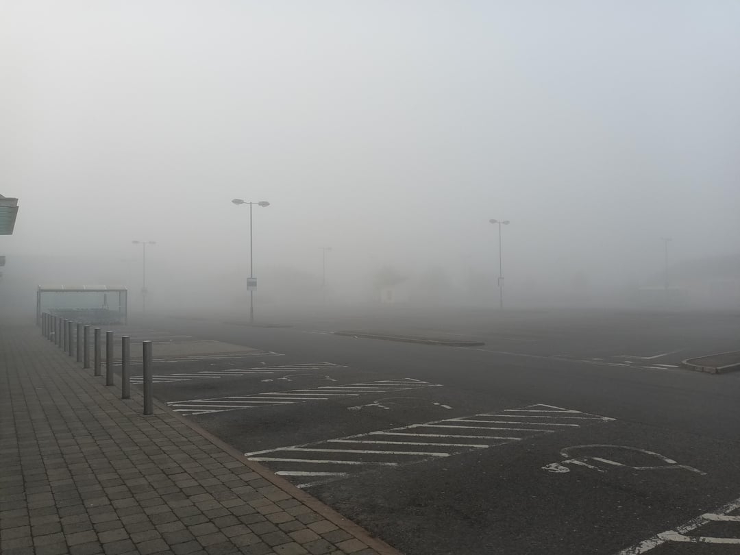 A foggy, empty parking lot with dimly visible streetlights and pavement lines