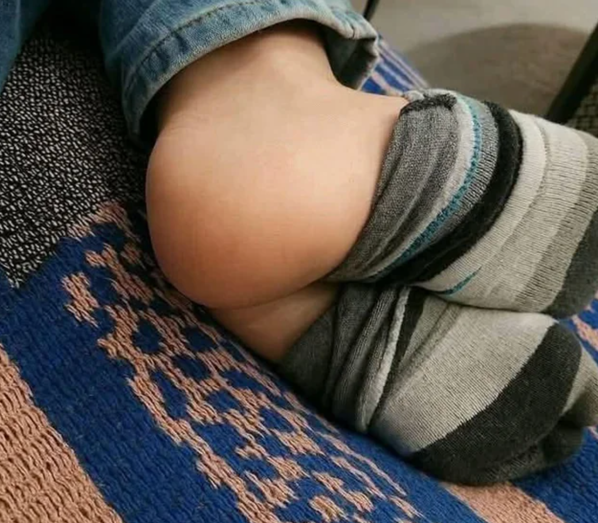 Person wearing mismatched striped socks on their feet while sitting cross-legged on a patterned blanket