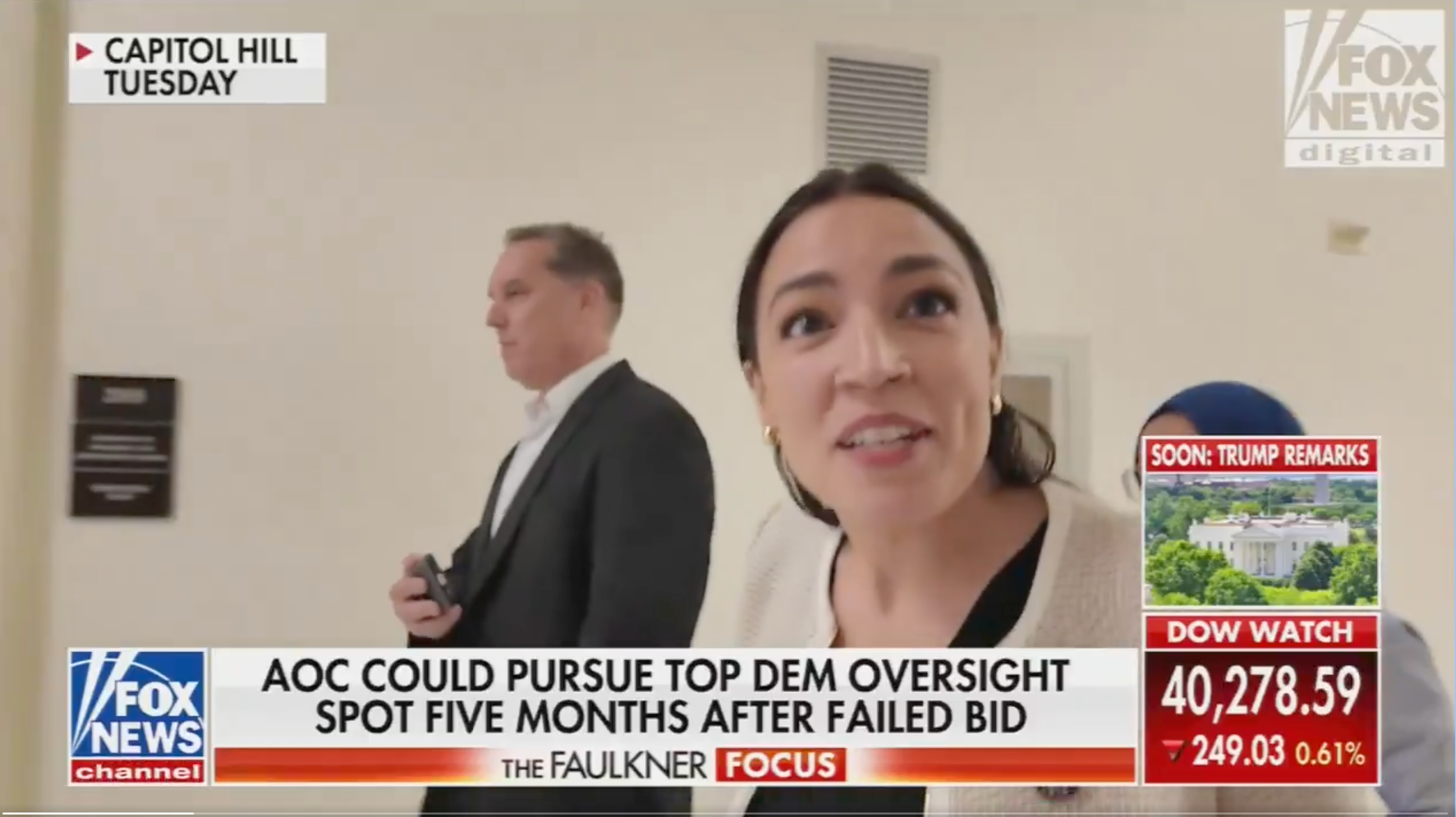 A person is walking in a hallway, looking toward the camera. A news headline suggests they might pursue a top Democratic oversight position