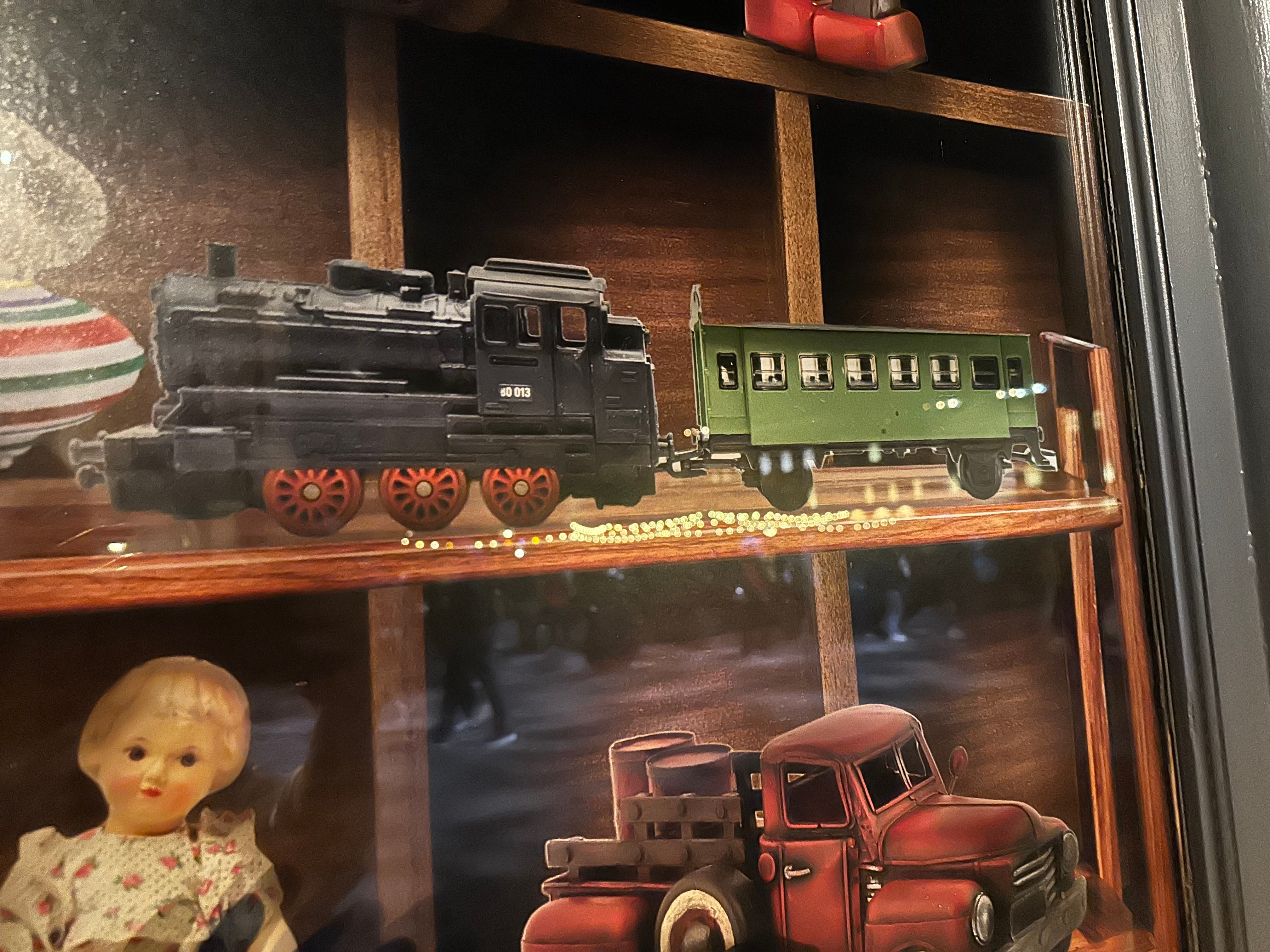 Toy train and vintage model truck displayed on a wooden shelf, with a doll nearby