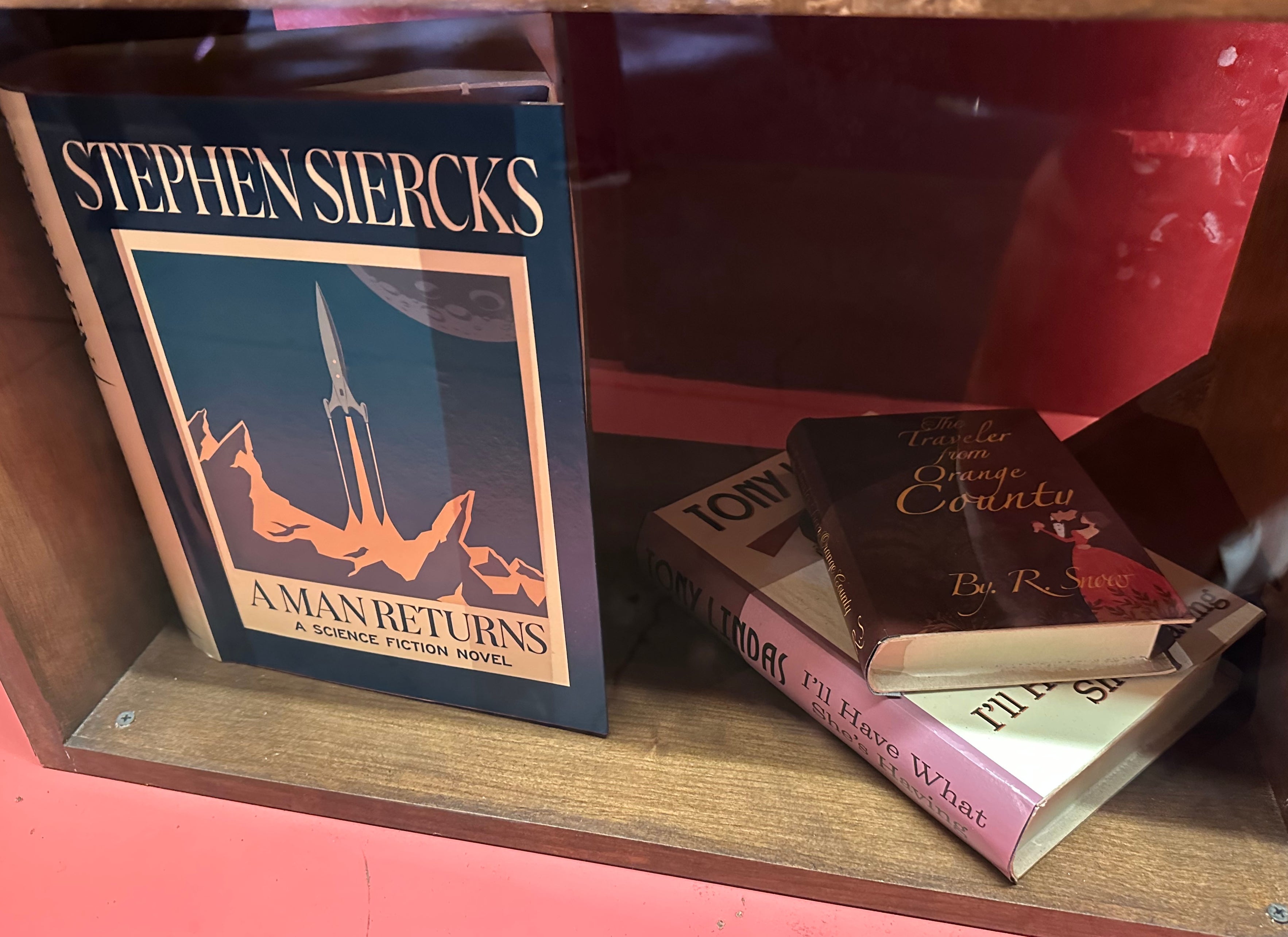 Books displayed in a wooden case, featuring Stephen Siercks’ &quot;A Man Returns,&quot; a sci-fi novel, alongside three other stacked books