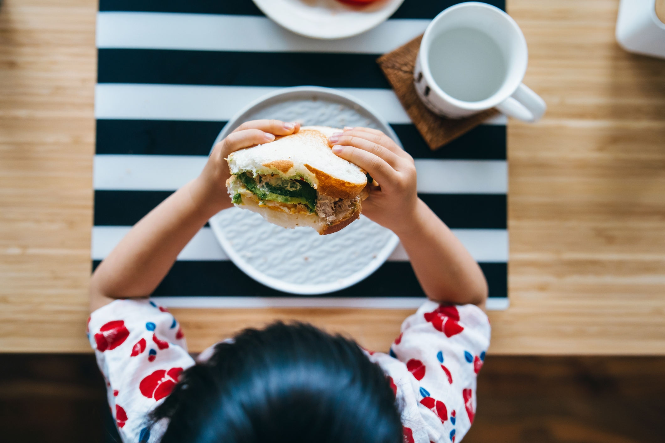 Barn som spiser en sandwich ved et bord sett med en drink og tallerkener, og støtter et sunt måltidsmiljø