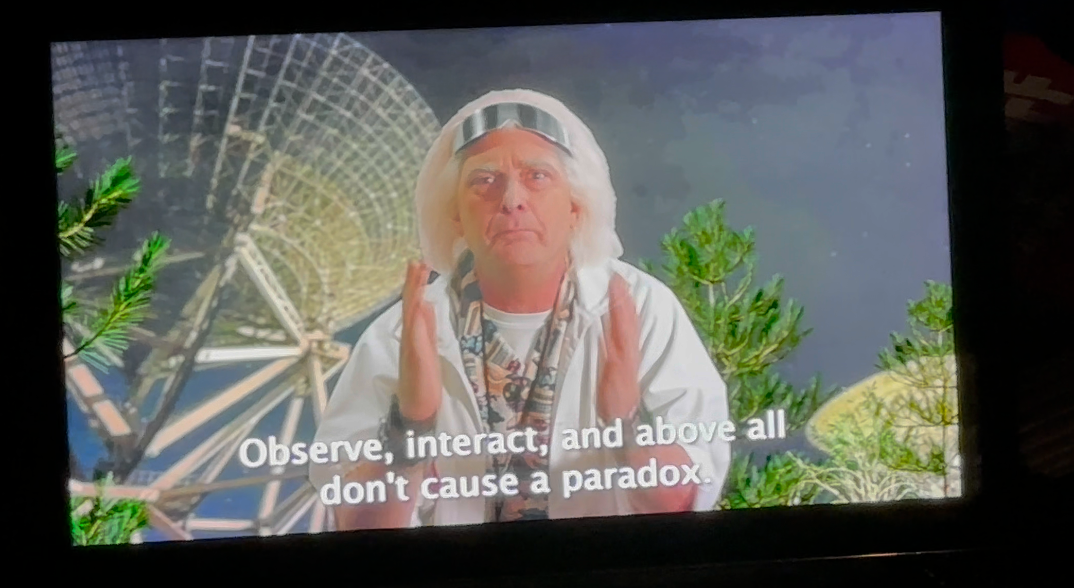 Man in sci-fi attire gestures, framed by satellite dishes and greenery. Subtitled: &quot;Observe, interact, and above all don't cause a paradox.&quot;