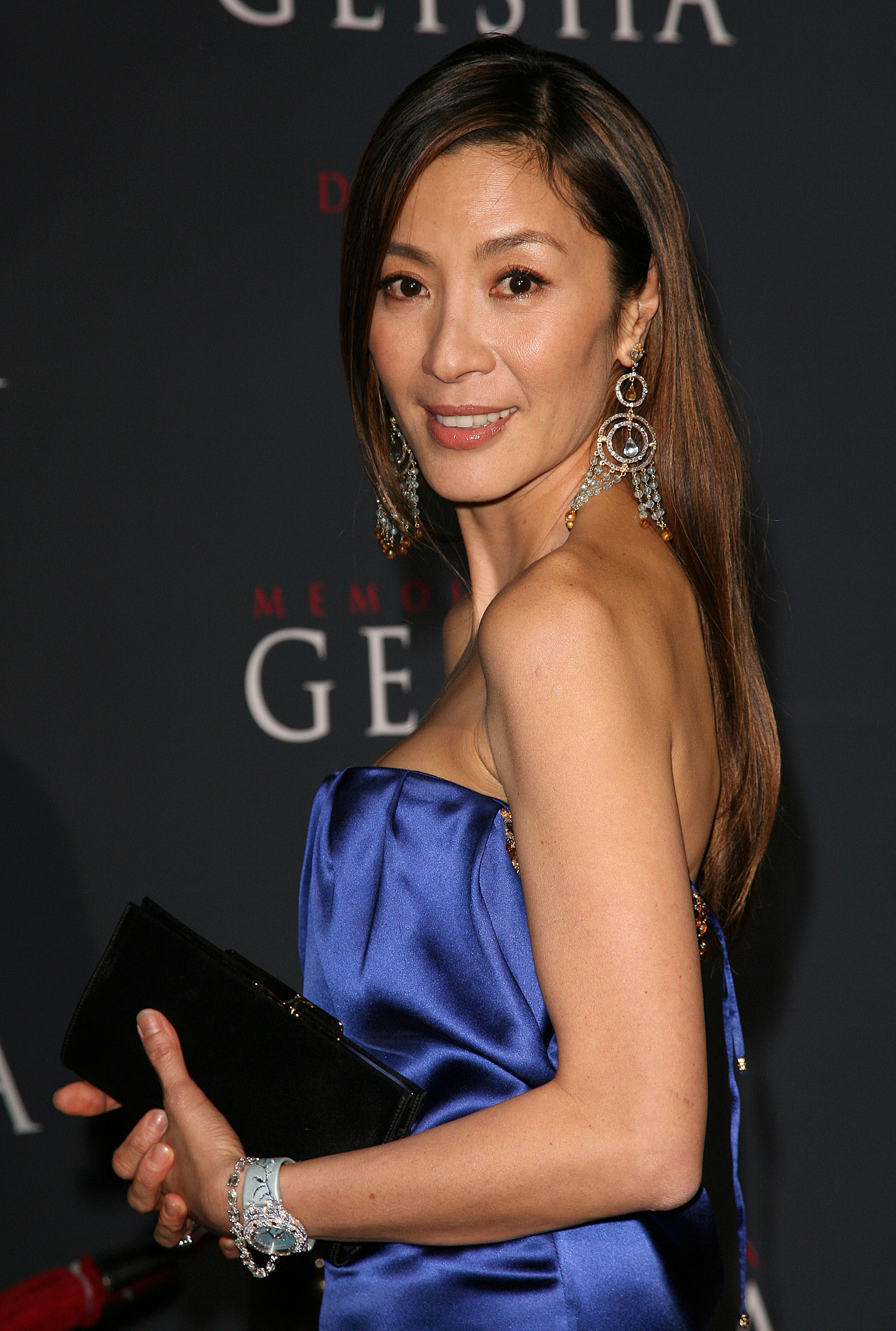 Person in elegant strapless dress, holding a clutch, poses on a red carpet at a 'Memoirs of a Geisha' event