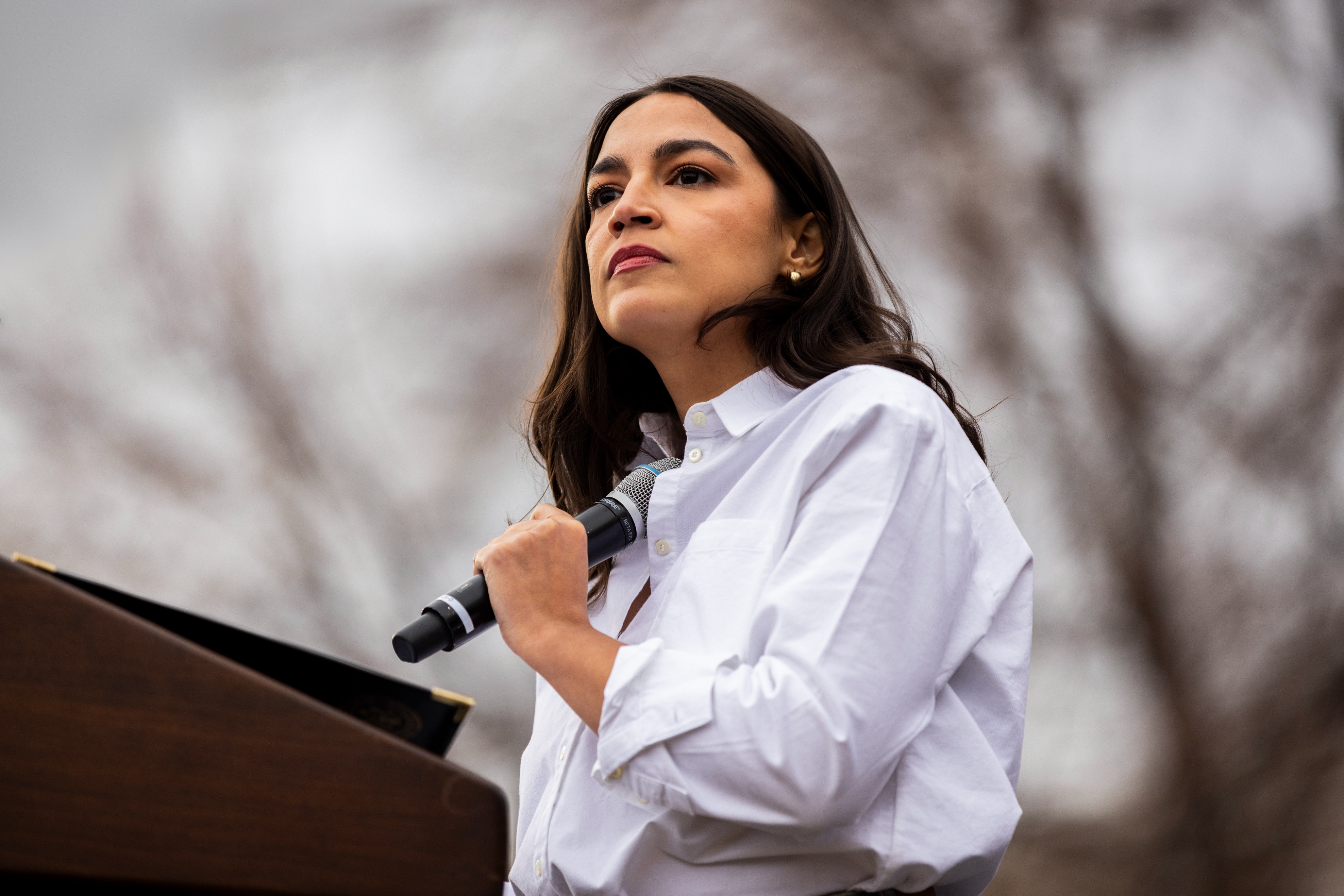 Person speaking passionately at an outdoor event, holding a microphone, wearing a white shirt